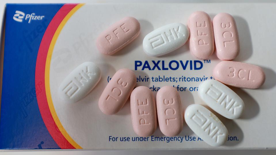 box of paxlovid with white and pink versions of pill scattered on top
